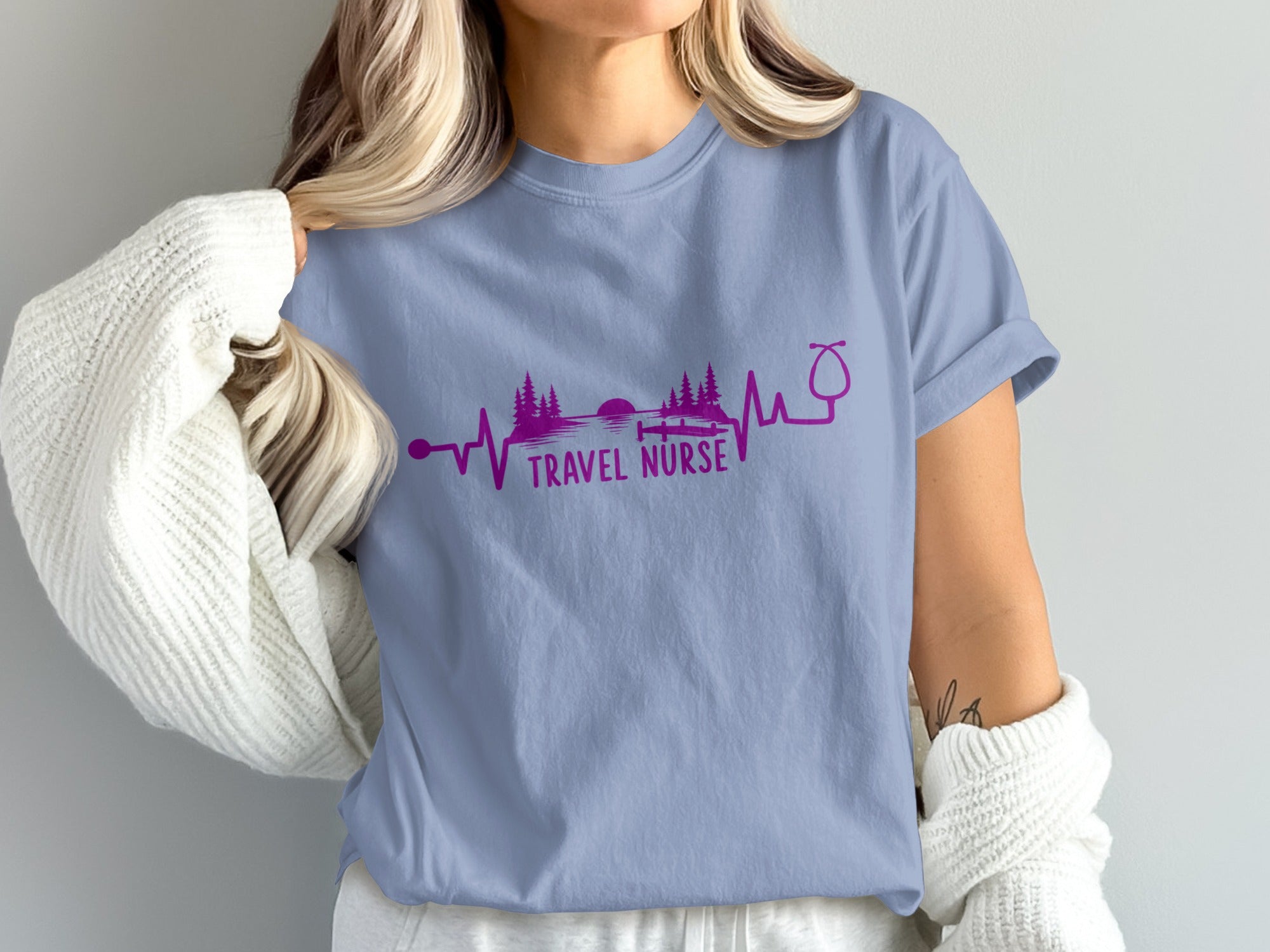 Purple stethoscope and heartbeat graphic above "TRAVEL NURSE" text on light blue shirt.