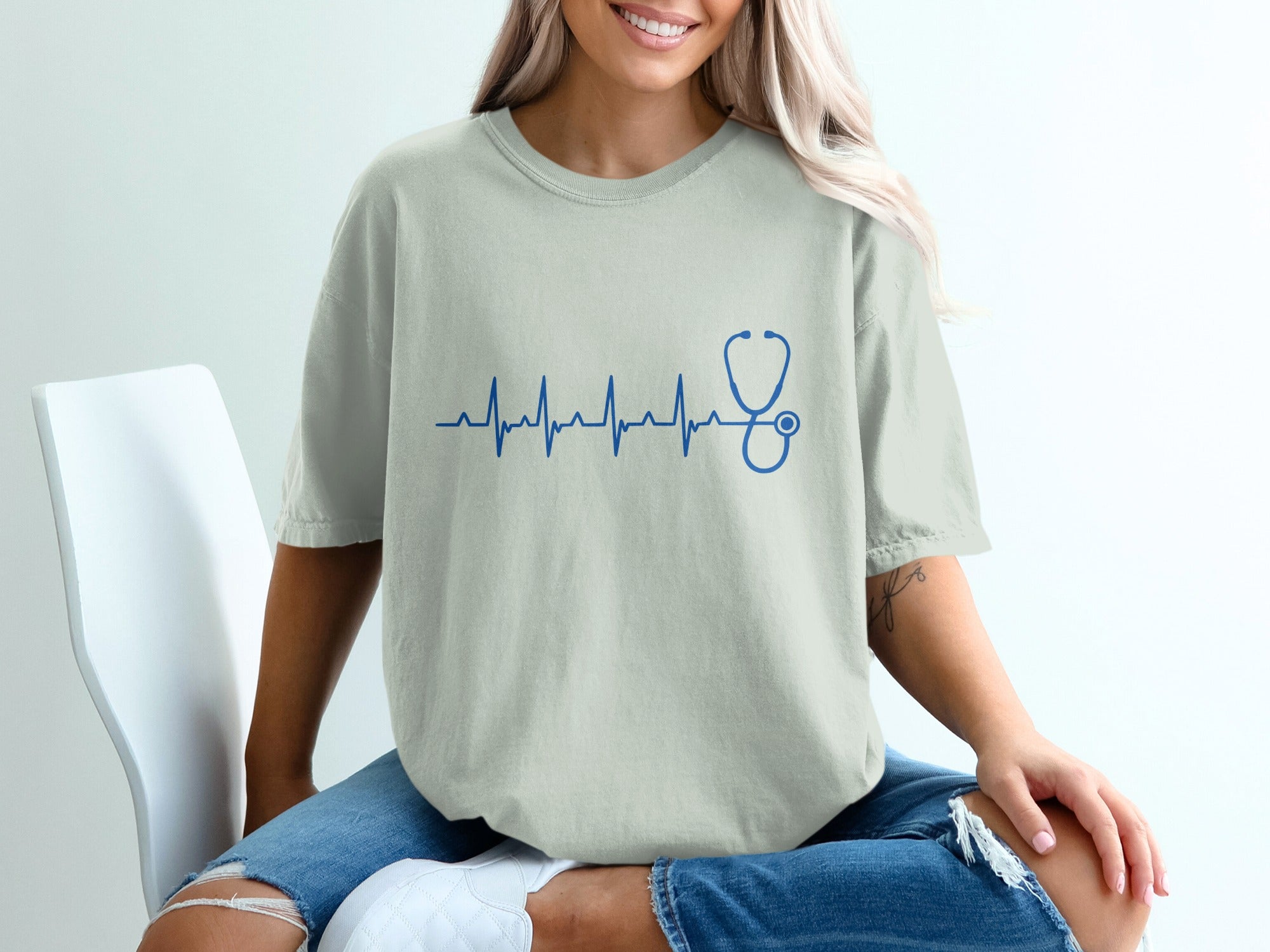 Cream t-shirt with a blue heartbeat and stethoscope graphic.