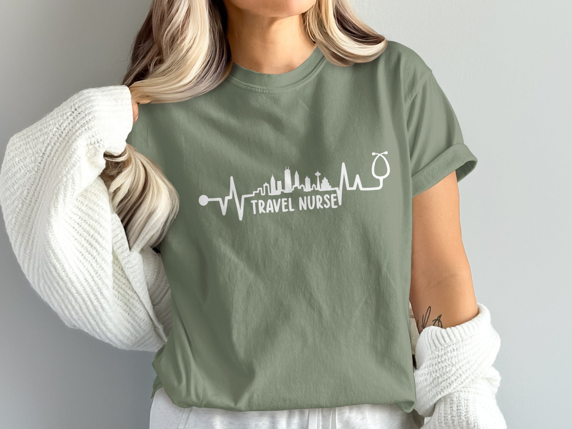 Olive green t-shirt with "TRAVEL NURSE" text and cityscape heartbeat design.