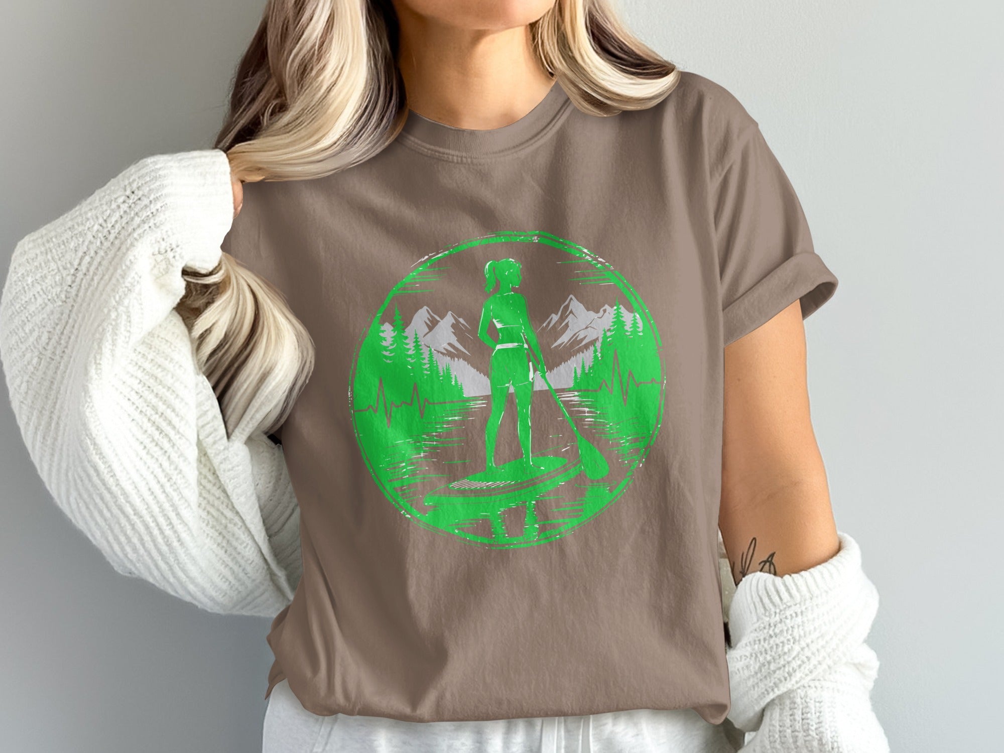 Woman in brown t-shirt with green paddleboarder and mountain graphic.
